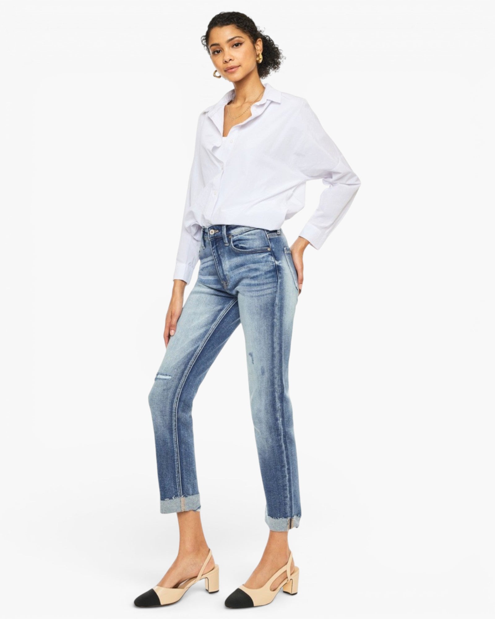 A model wearing a white long-sleeve button-up shirt, light-wash blue cropped jeans with rolled cuffs, and beige-and-black mule heels, posed against a plain white studio background.