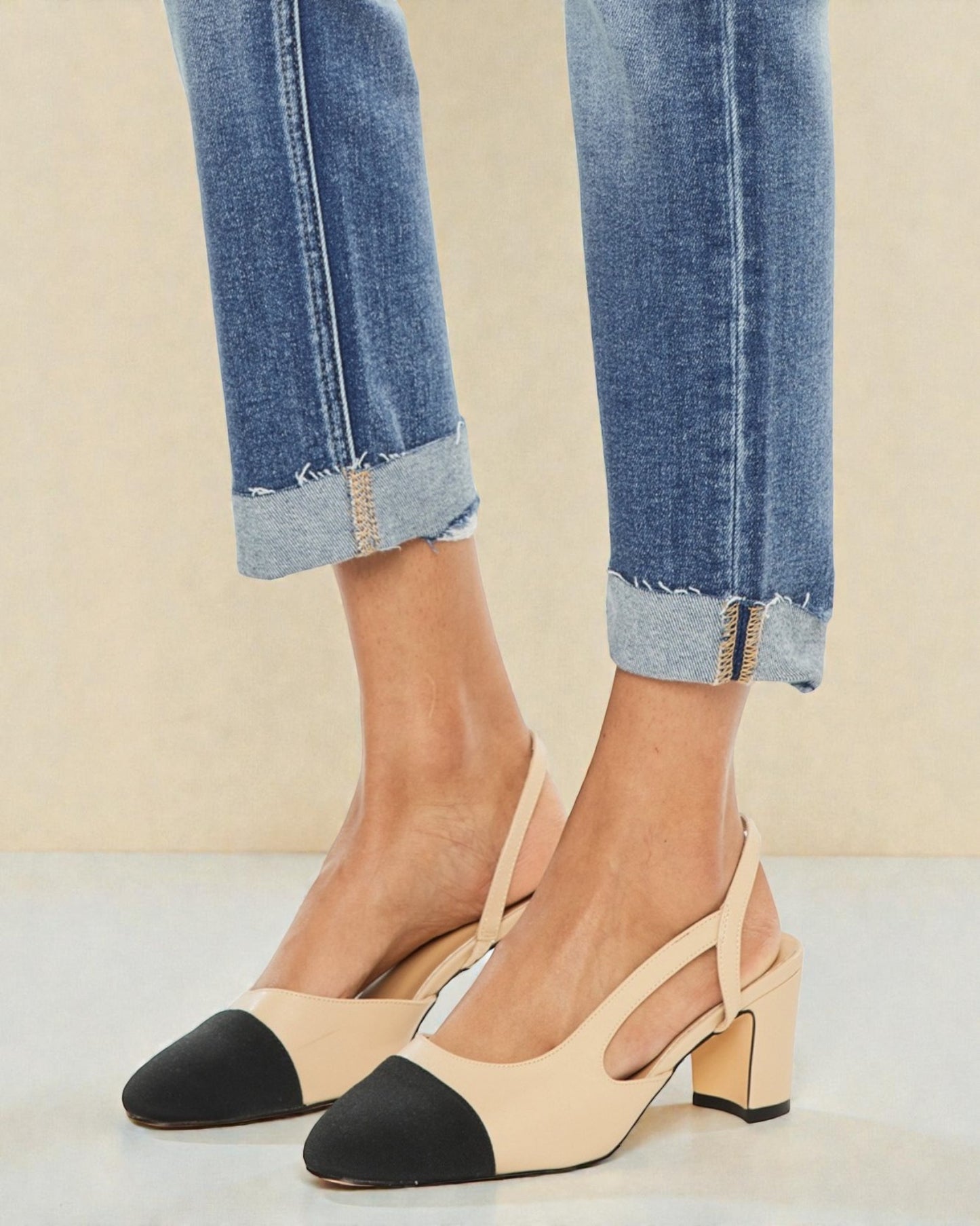 Beige and black shoes worn with rolled-up jeans on a neutral background