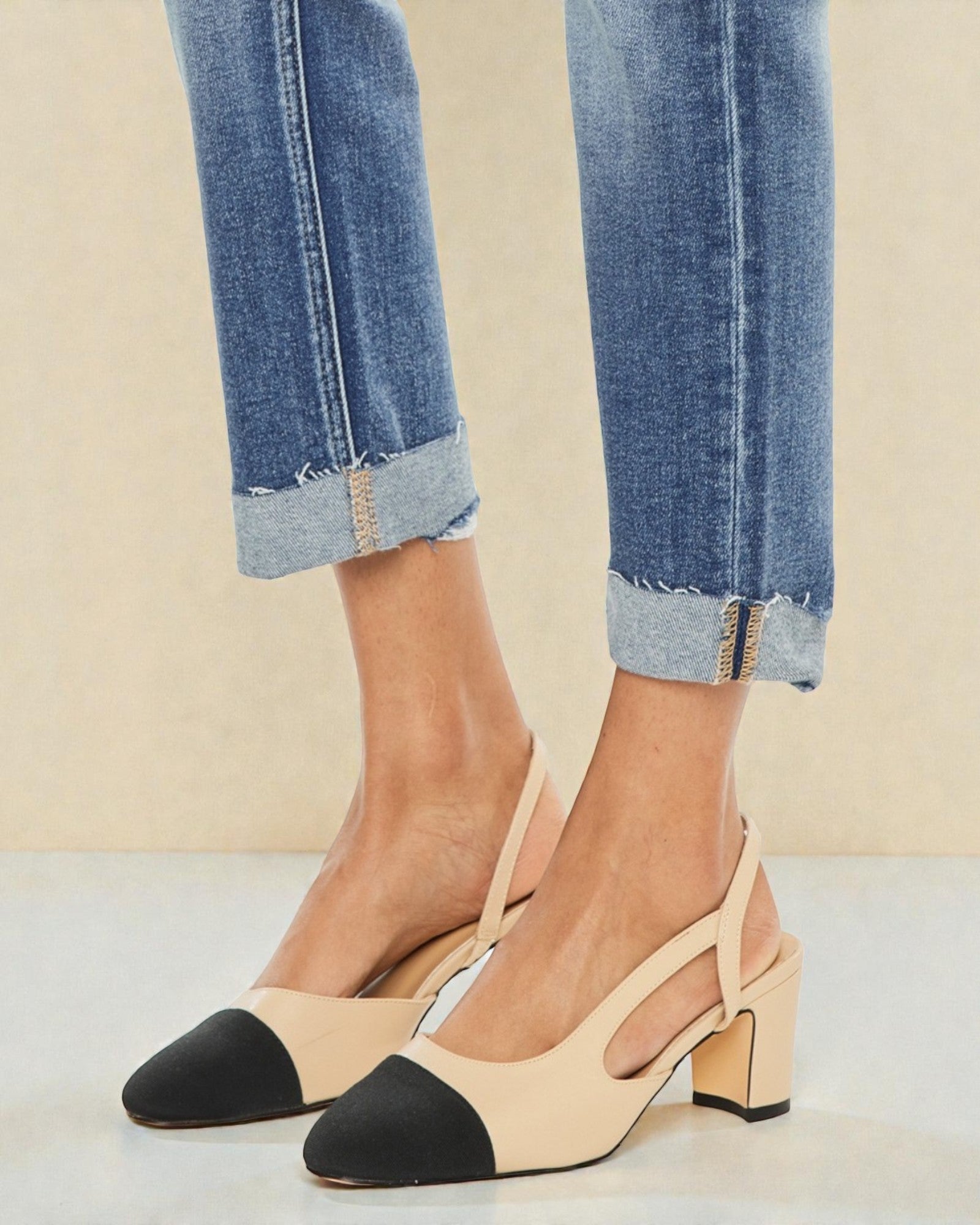 Beige and black shoes worn with rolled-up jeans on a neutral background