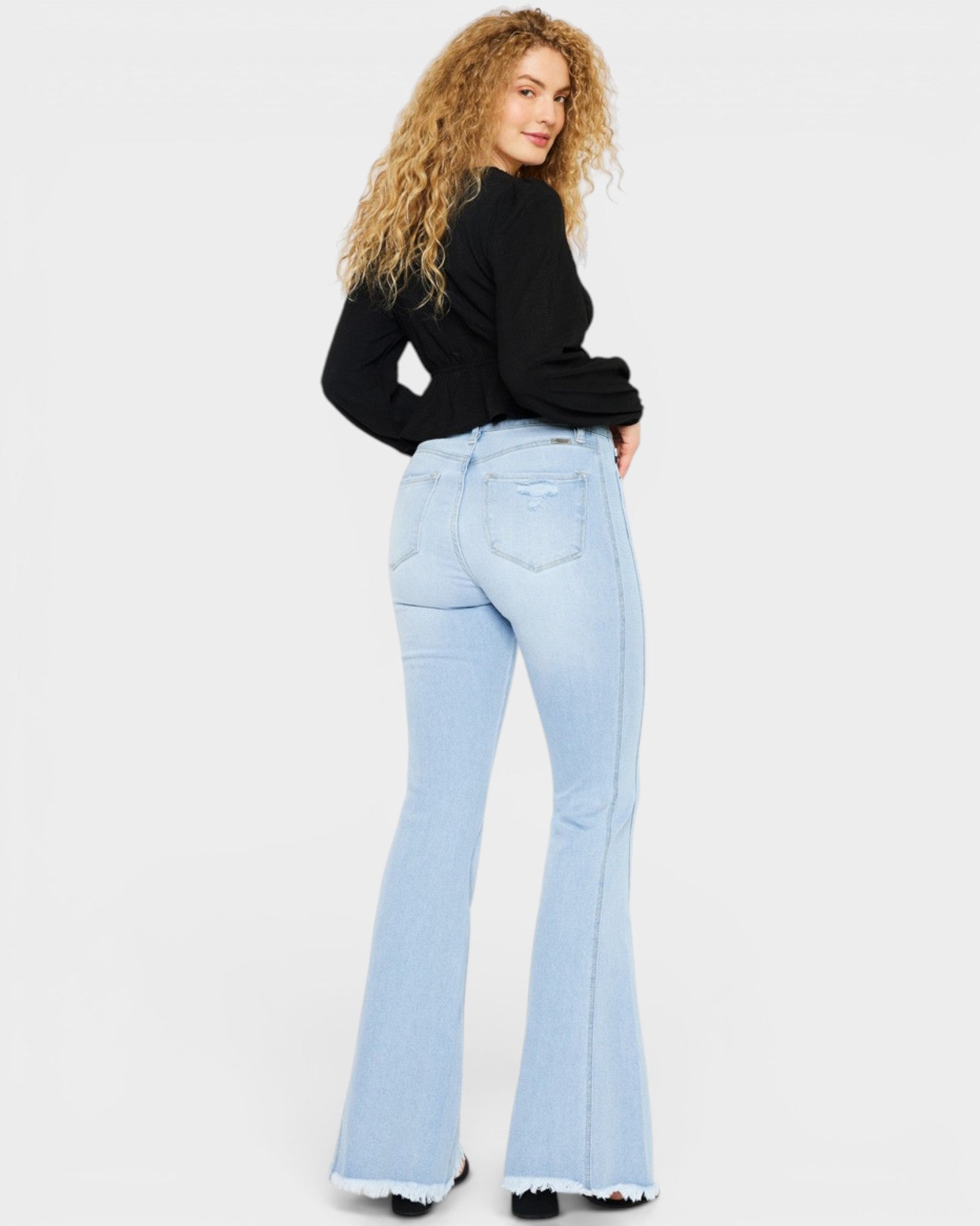 Woman wearing light blue flared jeans and a black top on a white background