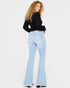 Woman wearing light blue flared jeans and a black top on a white background