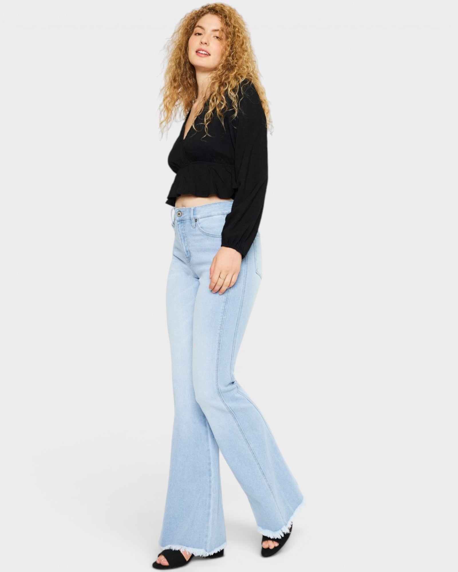 Woman wearing light blue flared jeans and a black top on a white background