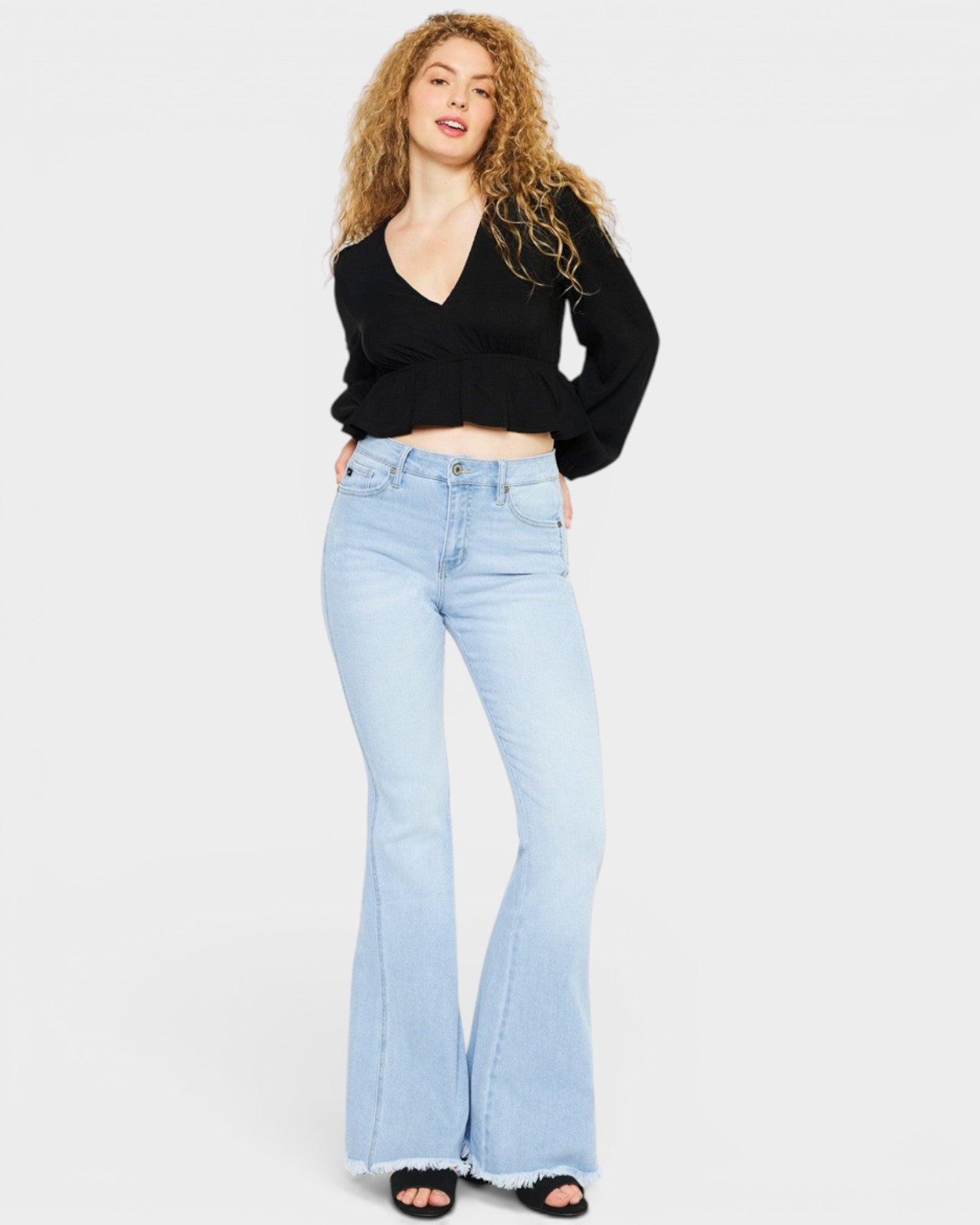 Woman wearing a black top and light blue flared jeans on a white background