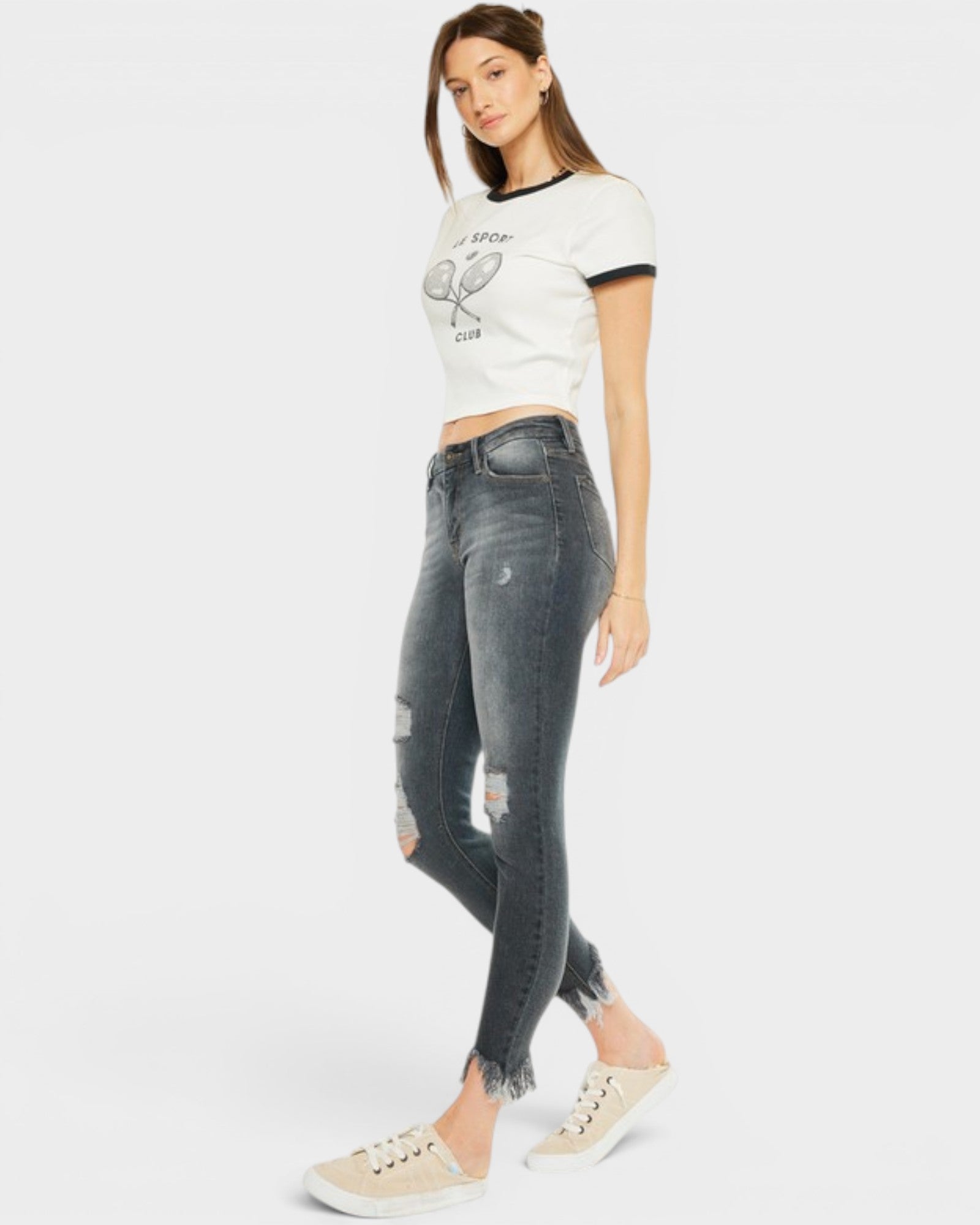 Woman wearing a white crop top with a graphic design and gray distressed jeans on a white background