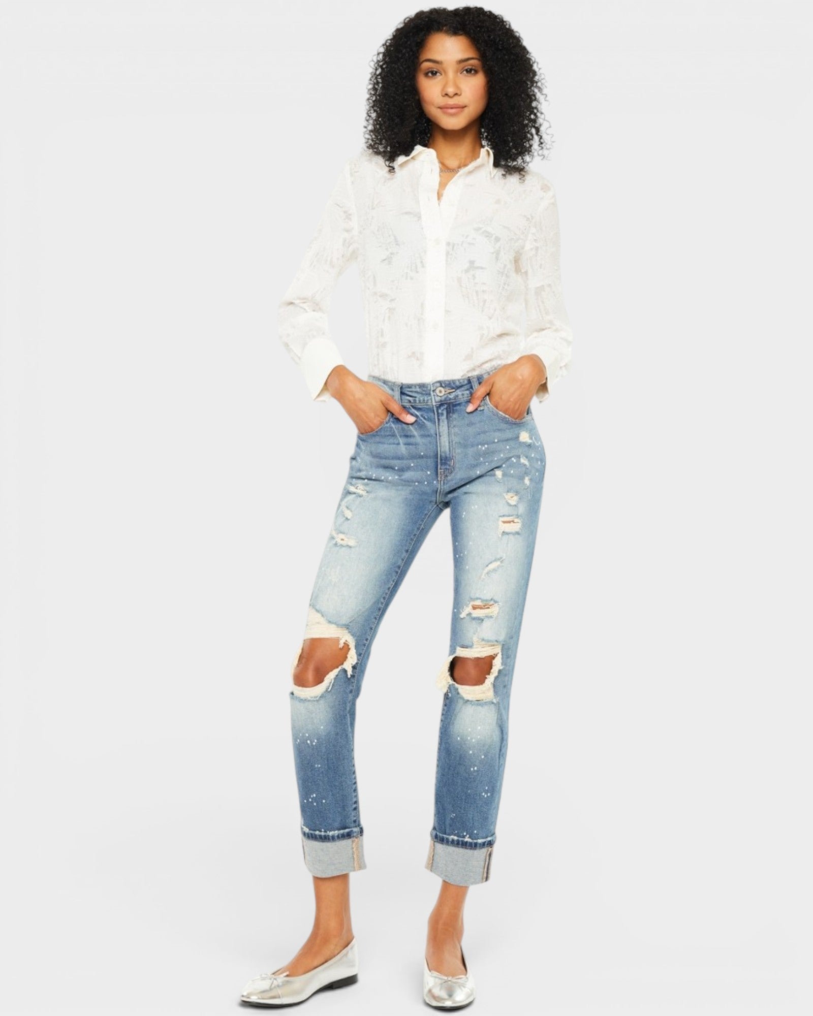 Woman wearing a white blouse and distressed blue jeans on a plain background