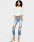 Woman wearing a white blouse and distressed blue jeans on a plain background