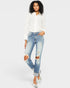 Woman wearing a white lace top and ripped blue jeans on a white background