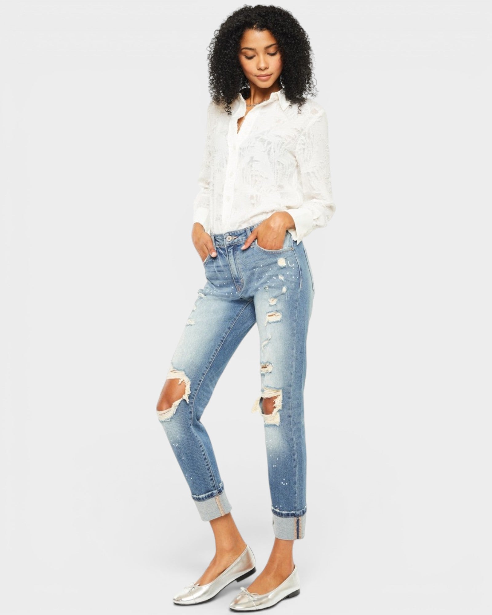 Woman wearing a white blouse and distressed blue jeans on a plain background