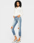 Woman wearing a white blouse and distressed blue jeans on a plain background