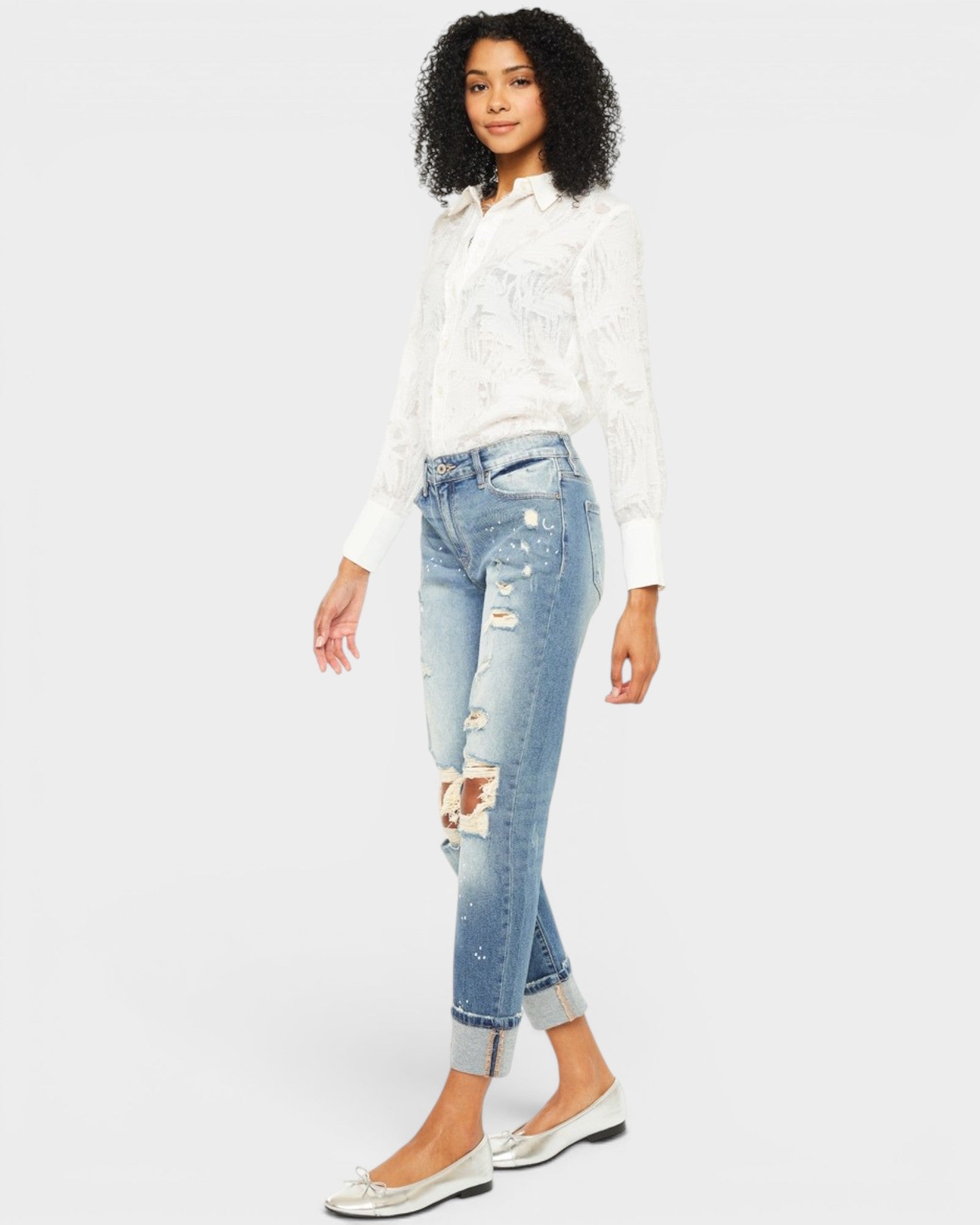 Woman wearing a white blouse and distressed jeans on a plain background
