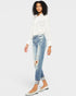 Woman wearing a white blouse and distressed jeans on a plain background