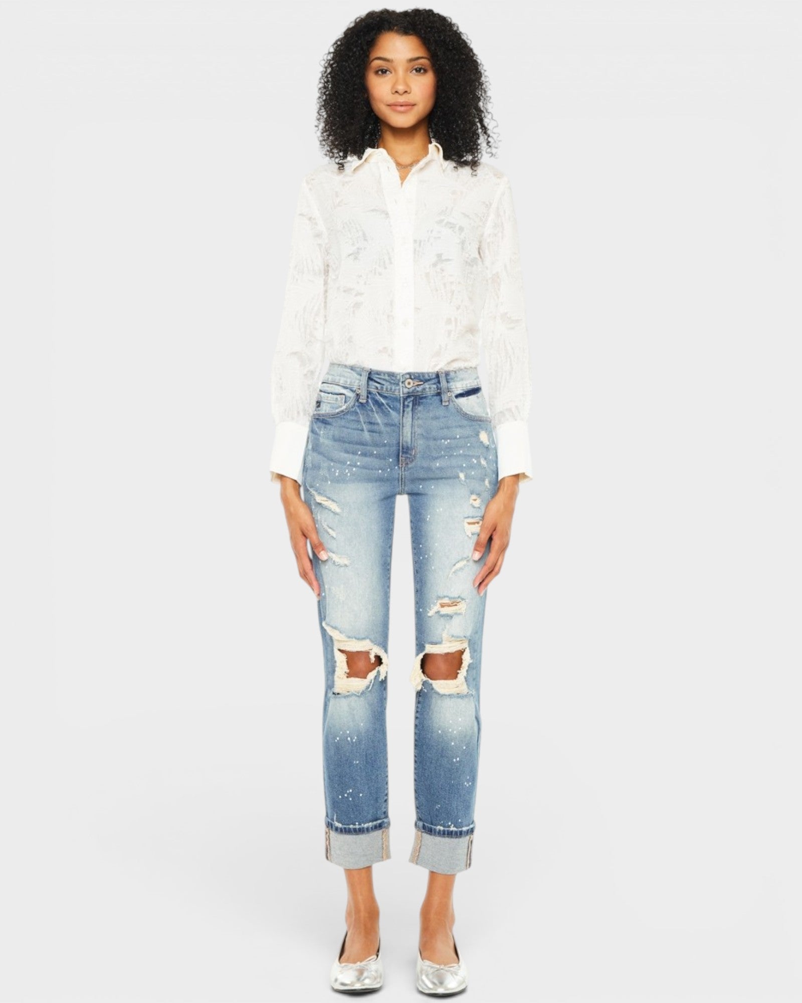 Woman wearing a white blouse and distressed blue jeans on a plain background