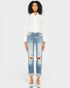 Woman wearing a white blouse and distressed blue jeans on a plain background