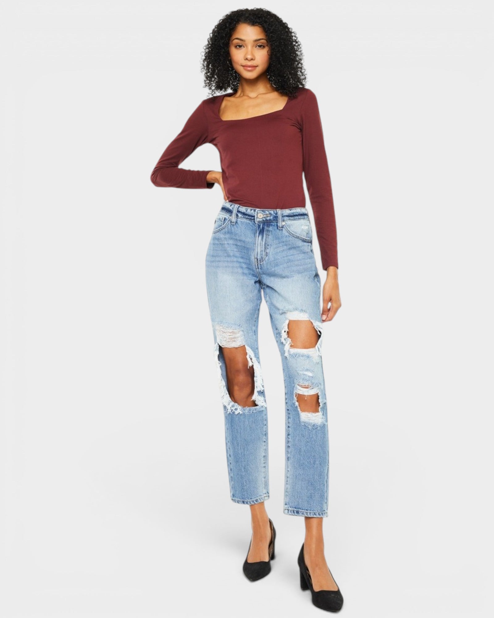 Woman wearing a burgundy long-sleeve top and ripped blue jeans on a white background