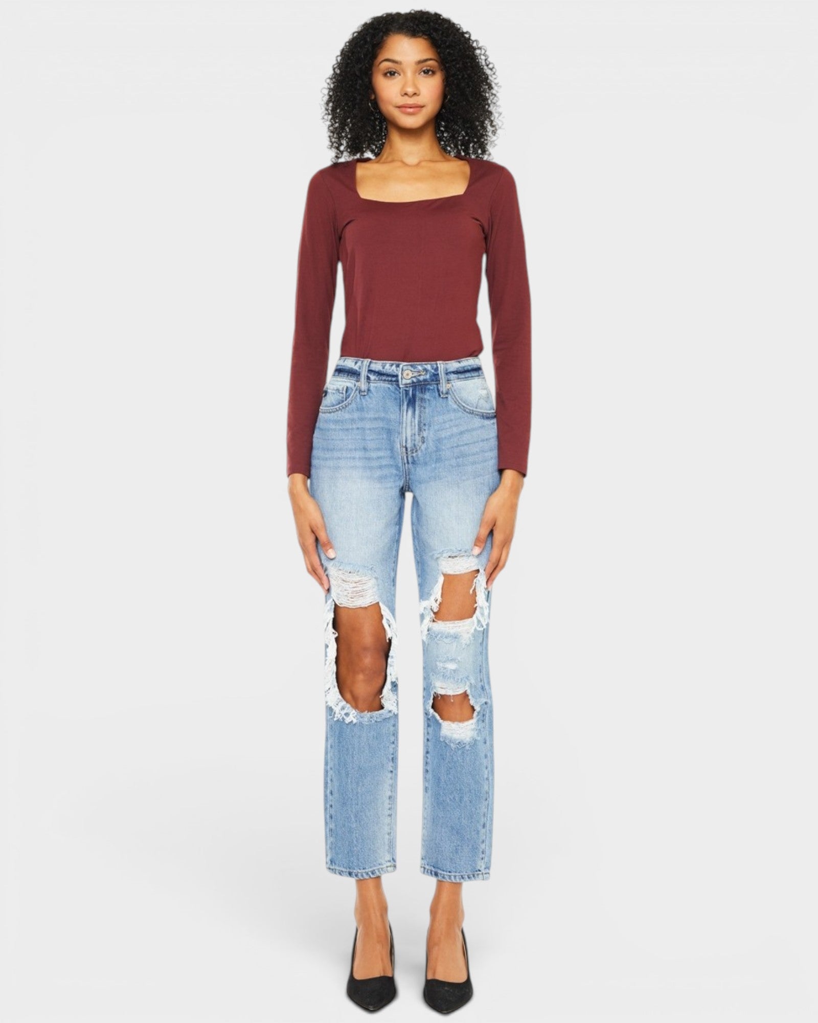 Woman wearing a burgundy long-sleeve top and light blue ripped jeans on a white background