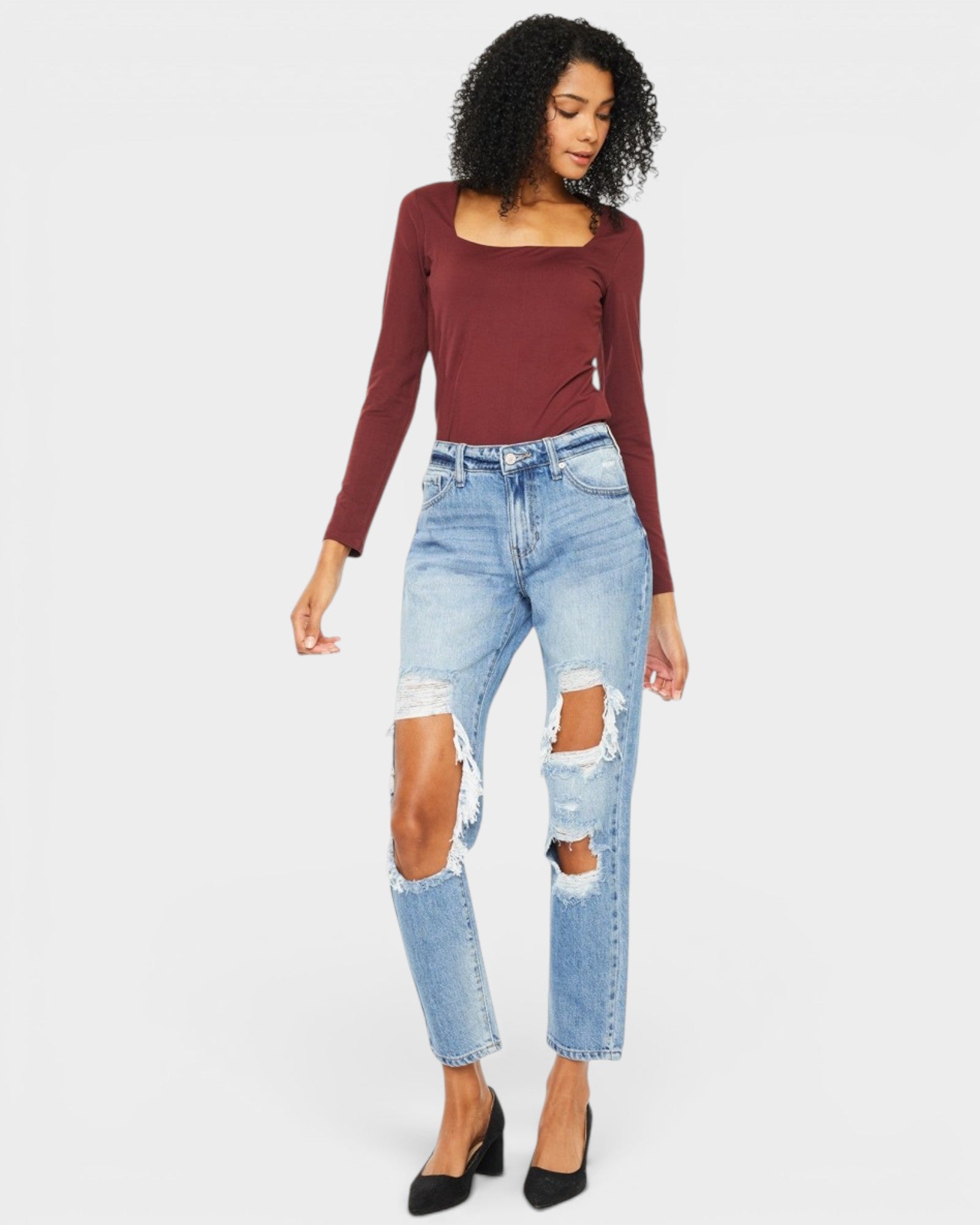 Woman wearing a burgundy long-sleeve top and ripped blue jeans on a white background