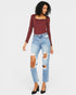 Woman wearing a burgundy long-sleeve top and ripped blue jeans on a white background