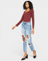 Woman wearing a burgundy long-sleeve top and light blue ripped jeans on a white background