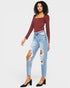 Woman wearing a burgundy long-sleeve top and ripped blue jeans on a white background