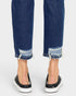 Close-up of blue jeans with frayed hems and black and white sneakers on a white background