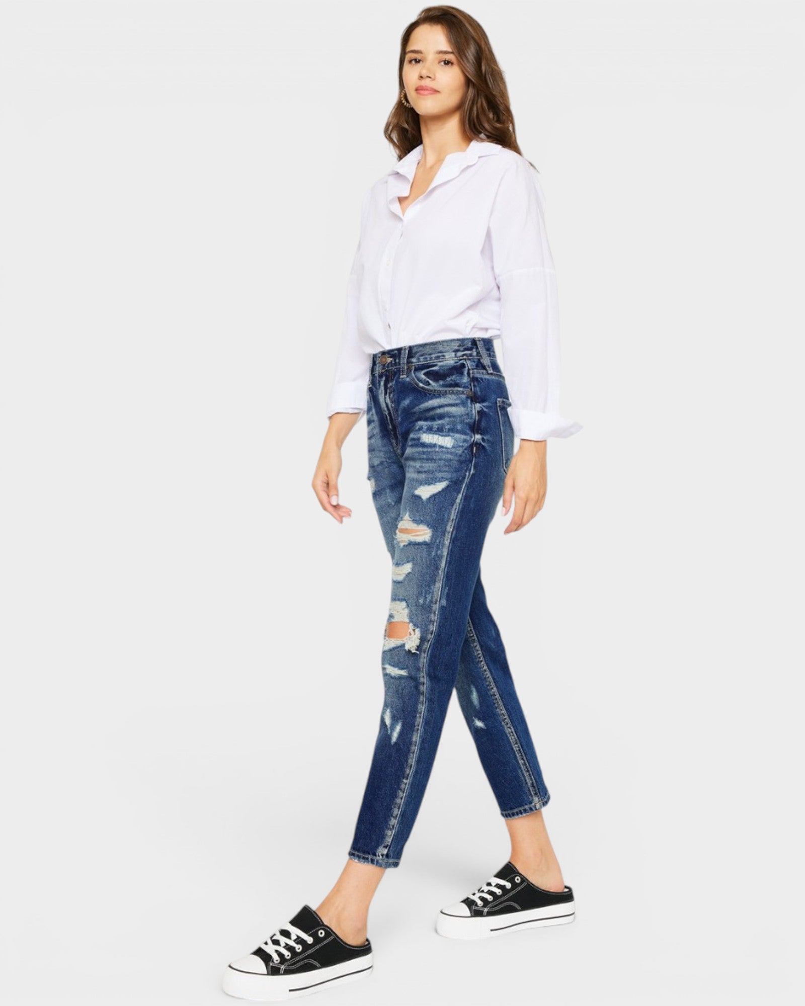Woman wearing a white shirt and blue distressed jeans on a white background