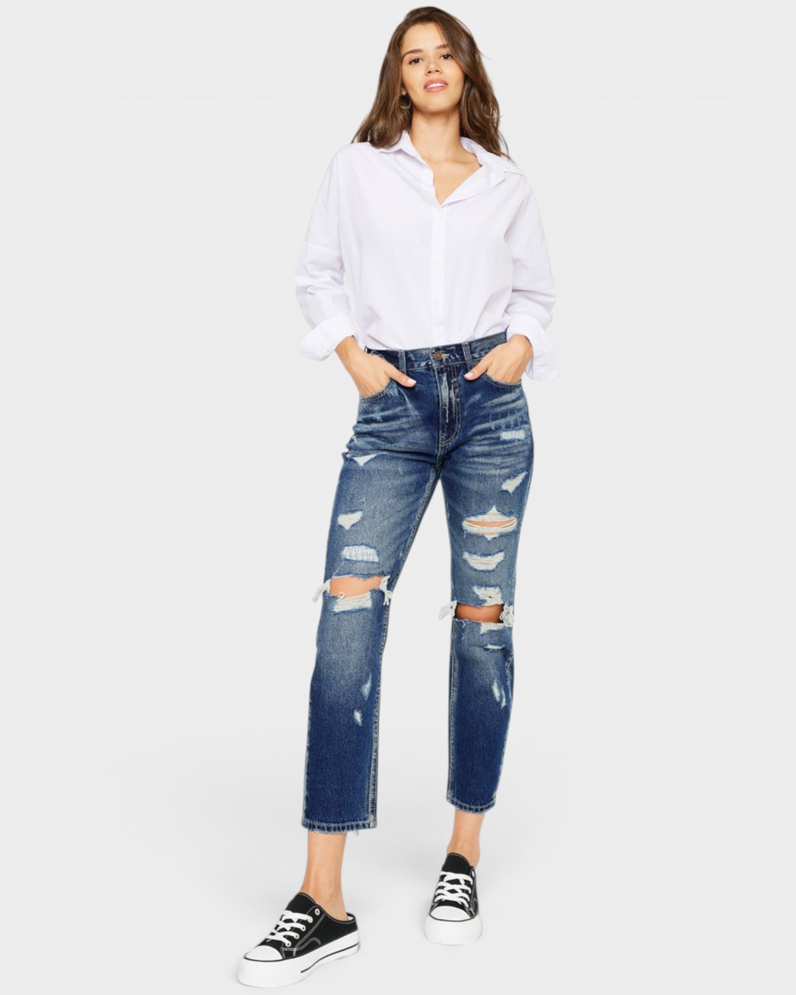 Woman wearing a white shirt and blue ripped jeans on a white background