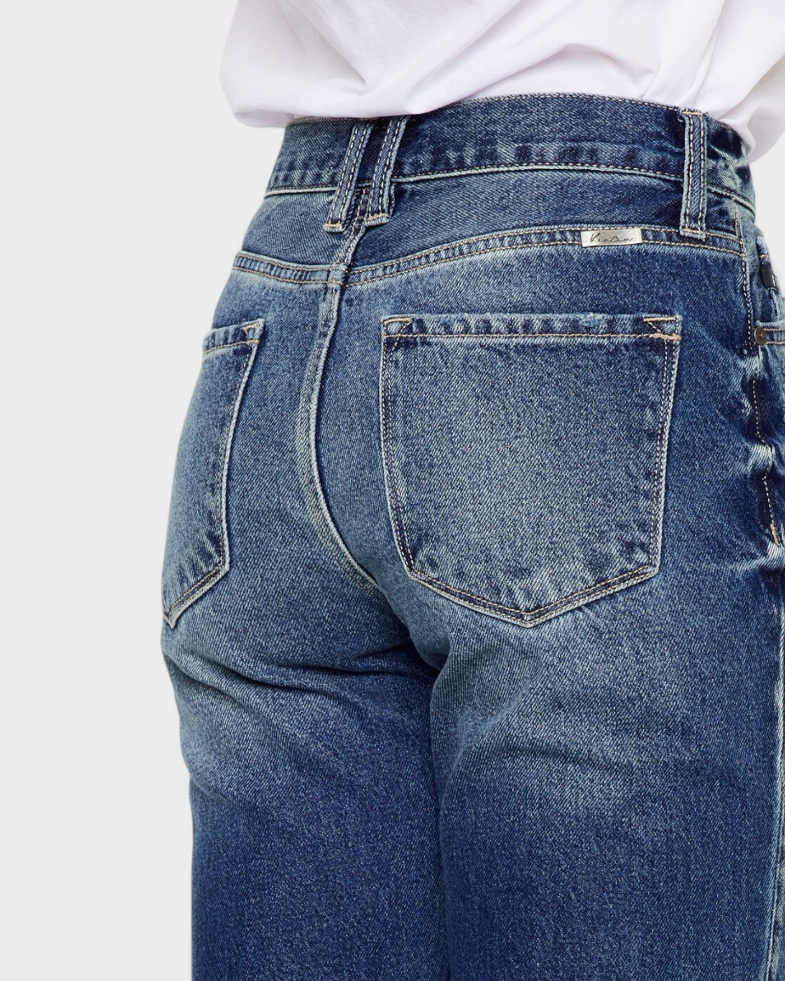 Close-up of blue jeans with a white shirt underneath on a light gray background