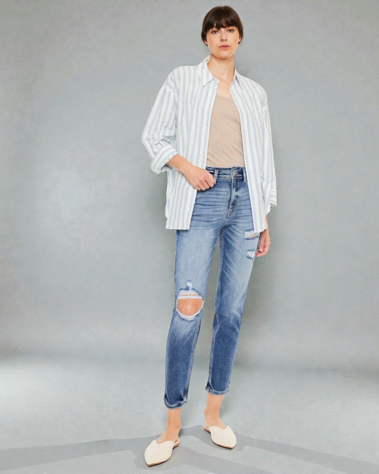 Person wearing a striped shirt, beige top, and ripped jeans on a gray background