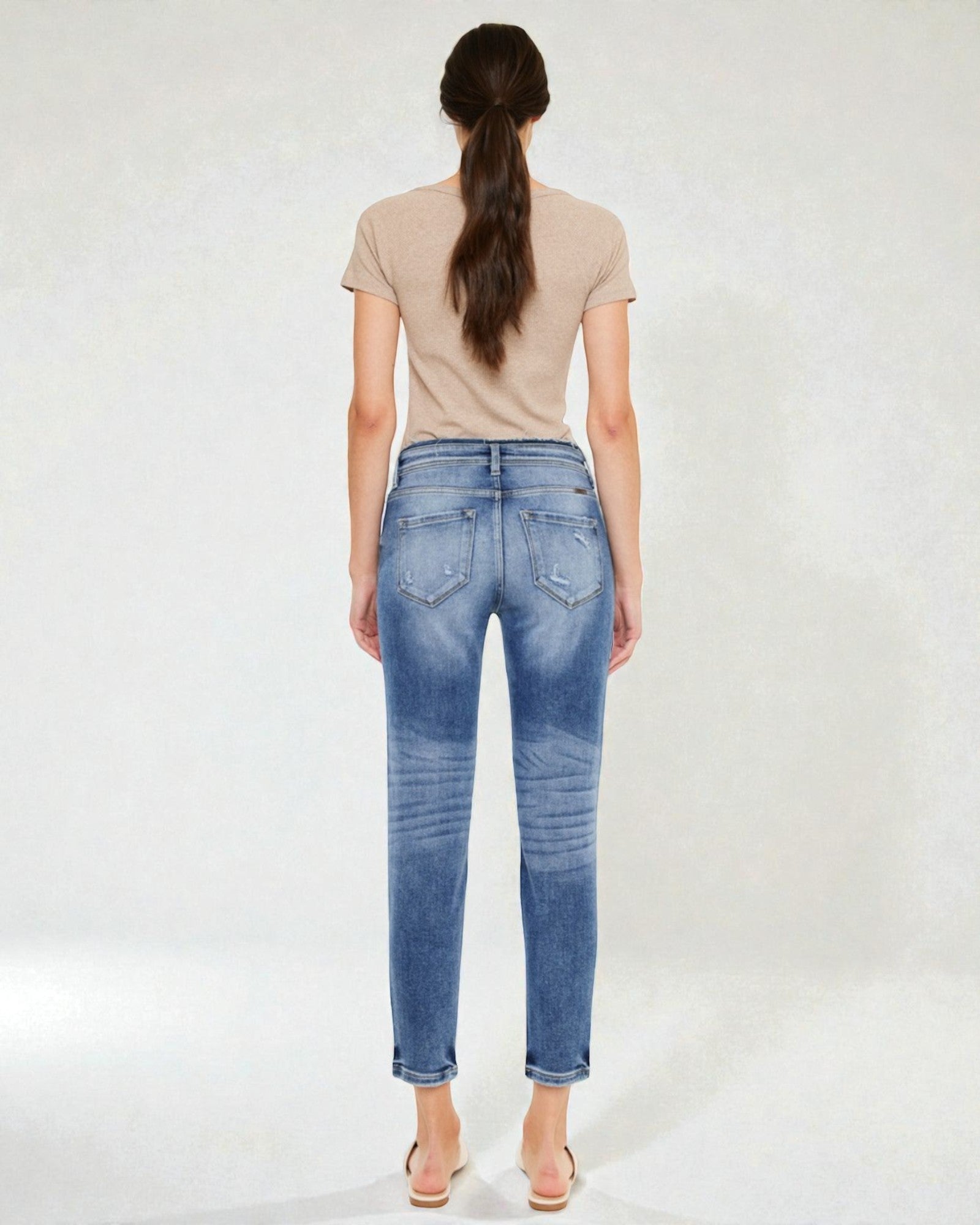Woman wearing blue jeans and a beige top on a white background