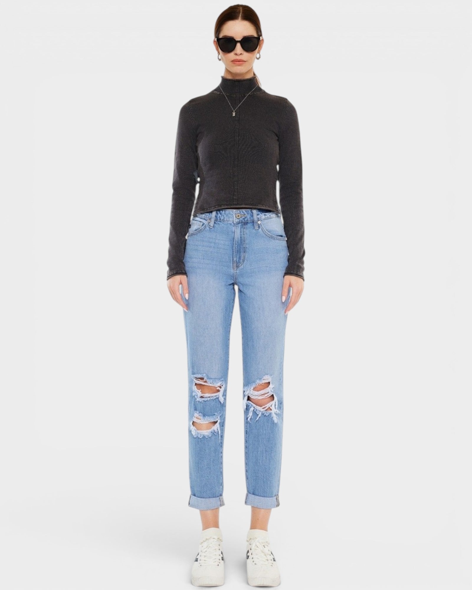 Person wearing a black turtleneck and light blue ripped jeans on a white background