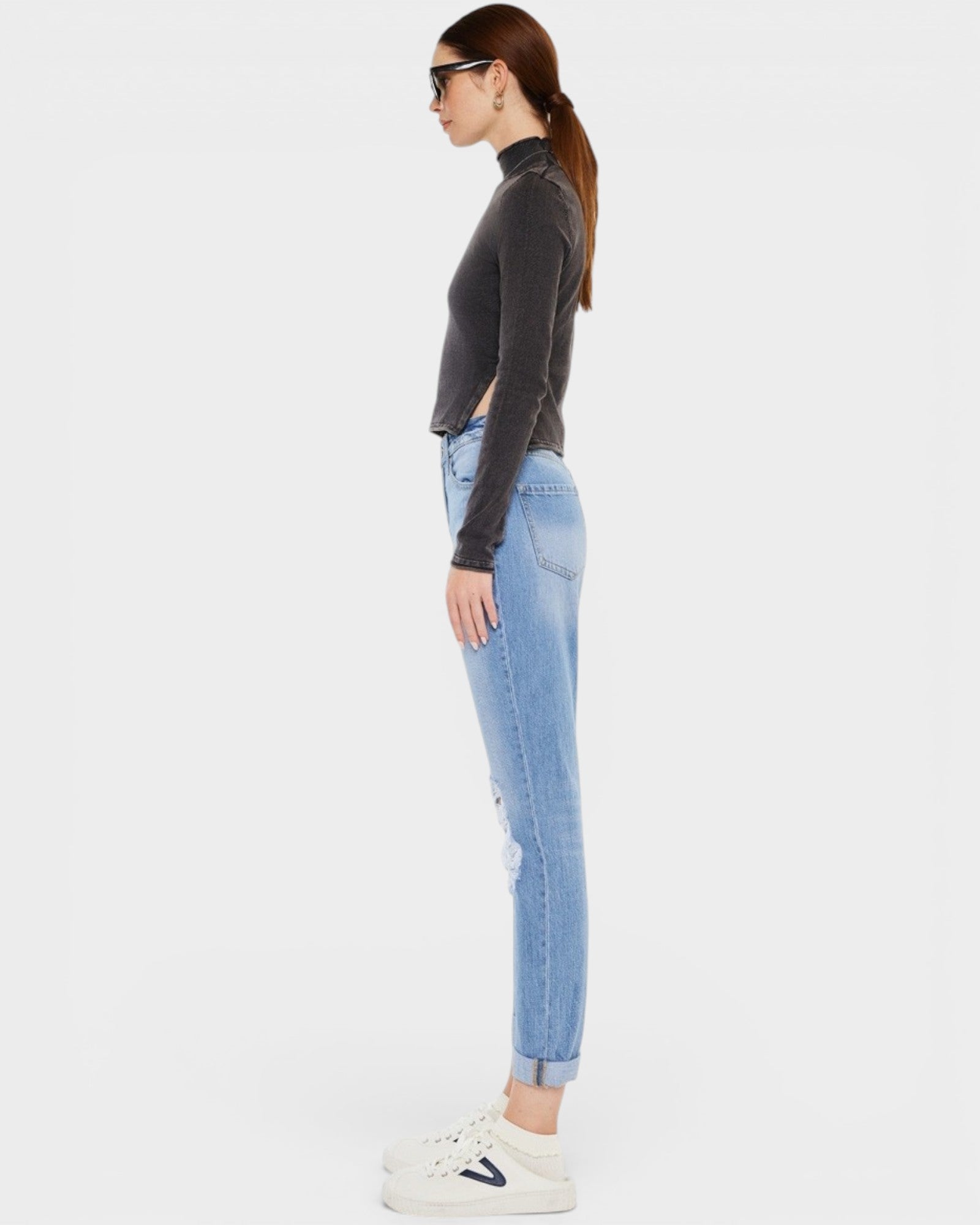 Woman wearing a dark gray turtleneck and light blue jeans on a white background