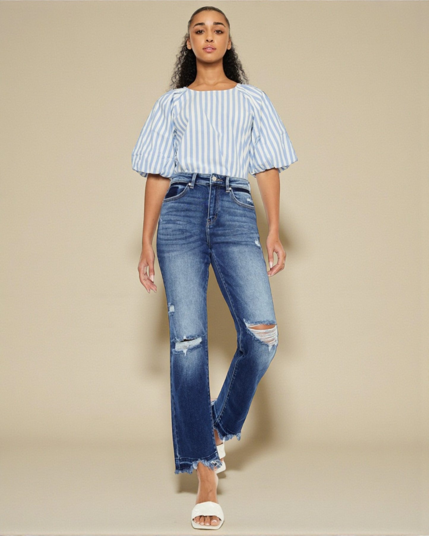 Woman wearing a striped top and distressed jeans on a beige background