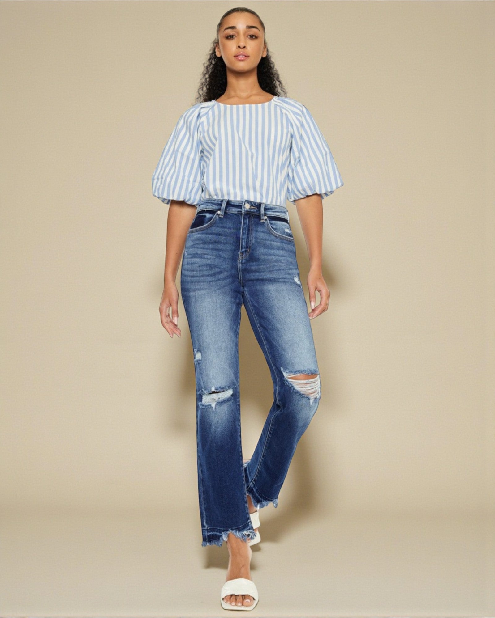 Woman wearing a striped top and distressed jeans on a beige background