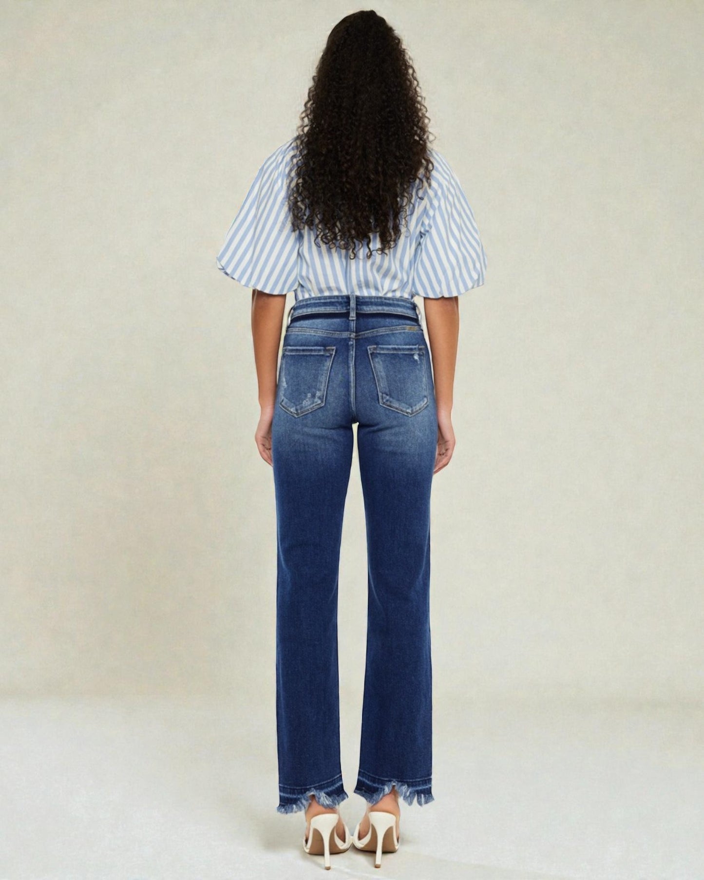 Person wearing blue jeans and a striped shirt from behind on a plain background
