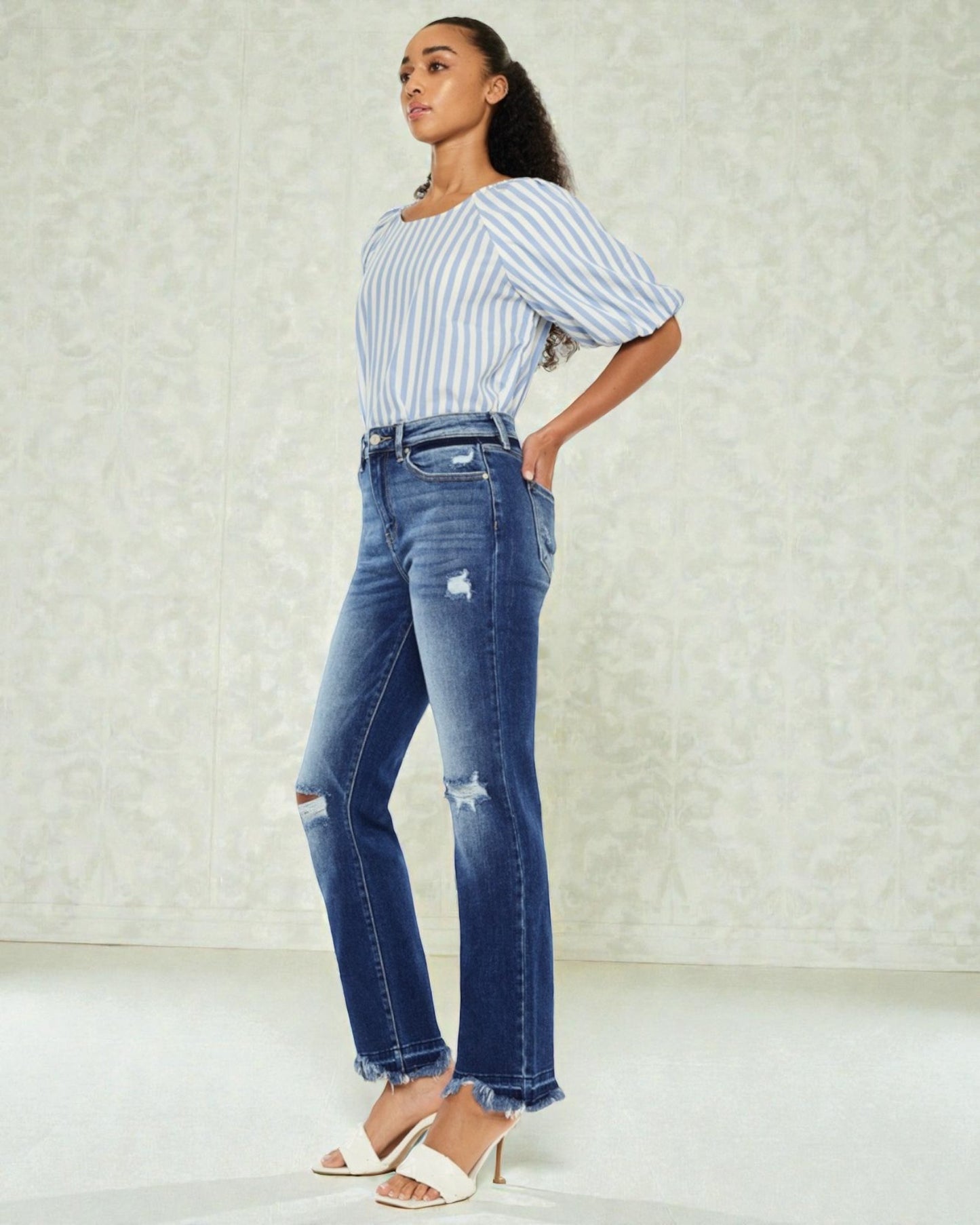 Woman wearing a striped shirt and blue jeans against a light background