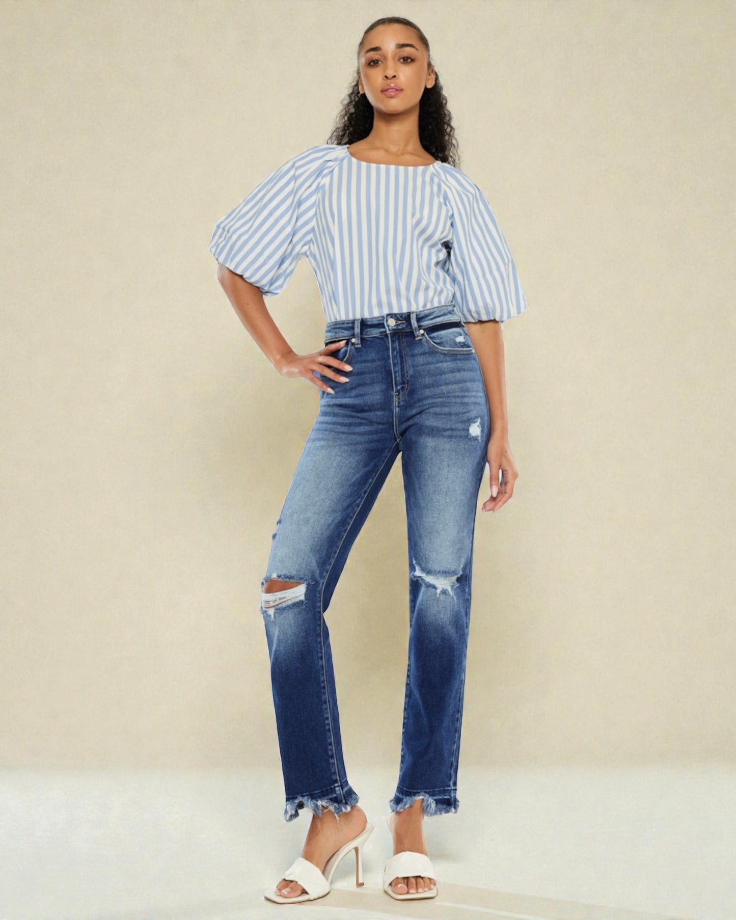 Woman wearing a striped blouse and distressed jeans against a beige background