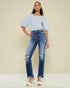 Woman wearing a striped blouse and distressed jeans against a beige background