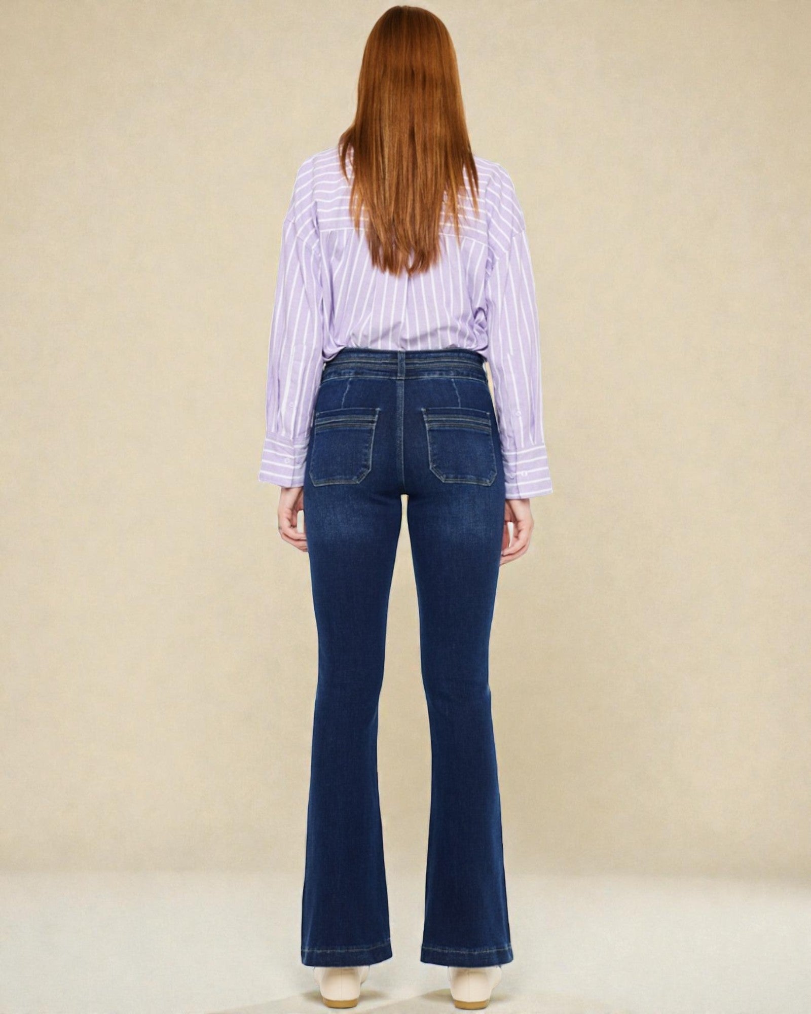 Person wearing blue flared jeans and a striped shirt from behind on a beige background