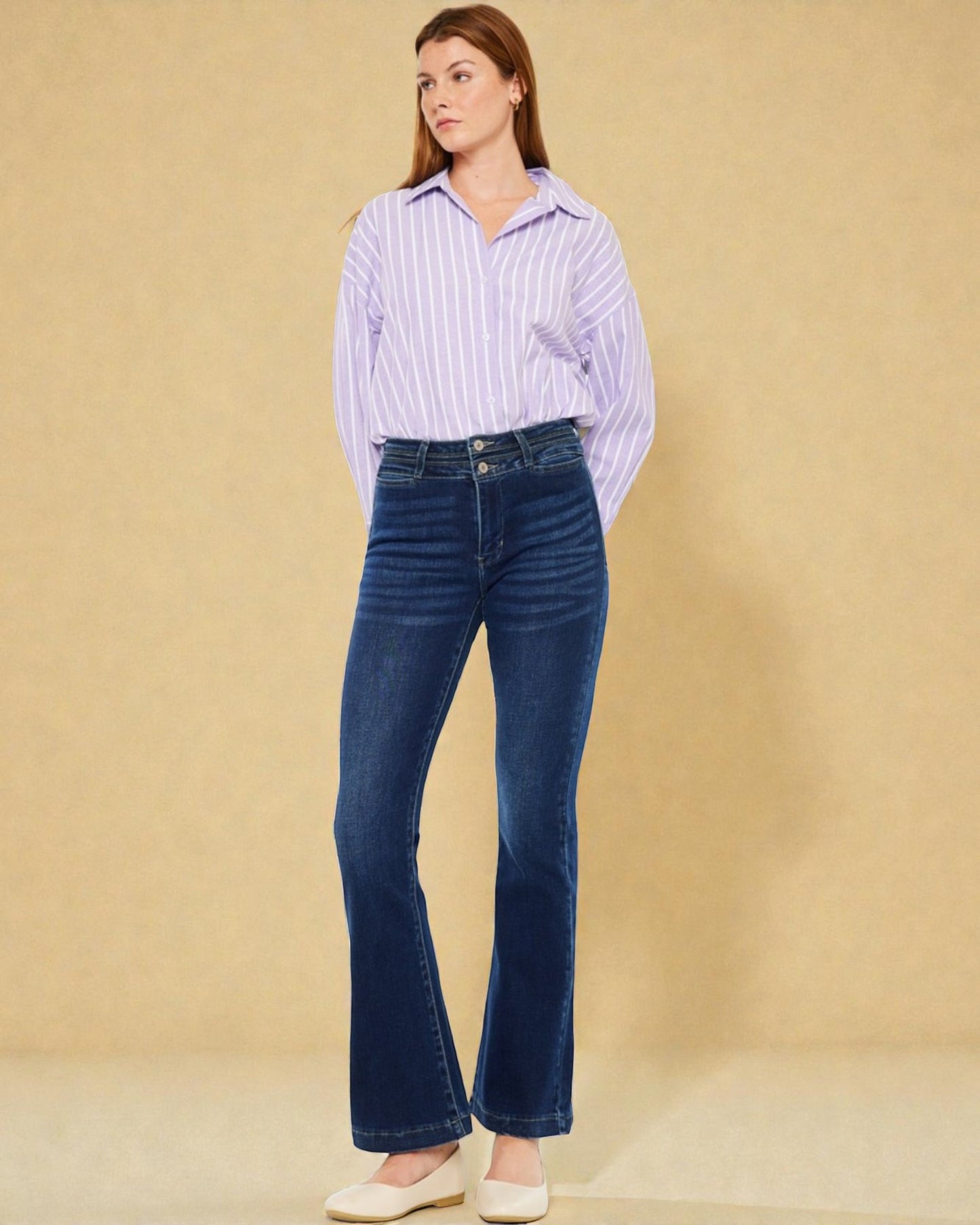 Woman wearing a striped shirt and blue jeans against a beige background