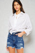 Woman wearing a white shirt and denim shorts against a plain background