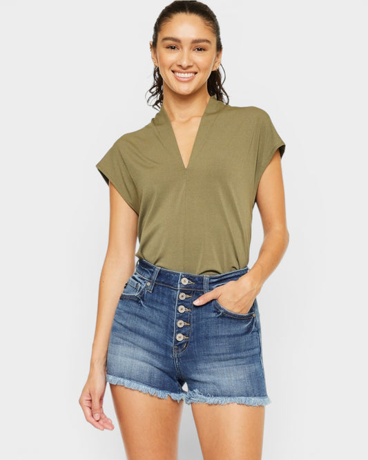 Woman wearing an olive green top and denim shorts on a white background