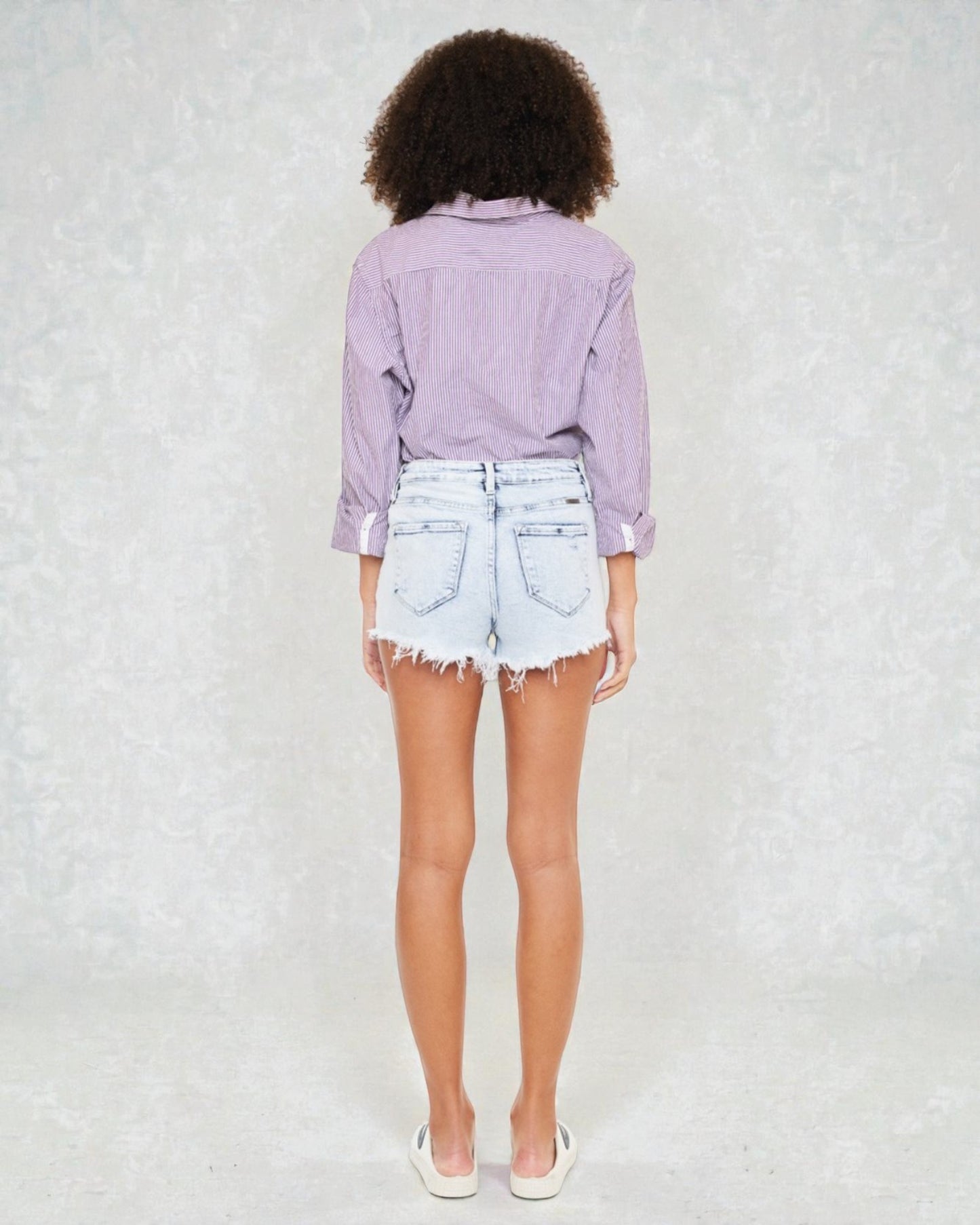 Person wearing a light purple shirt and denim shorts on a white background