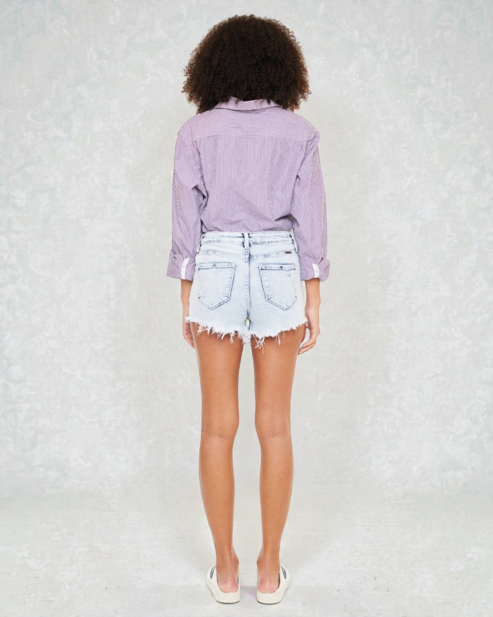 Person wearing a light purple shirt and denim shorts on a white background