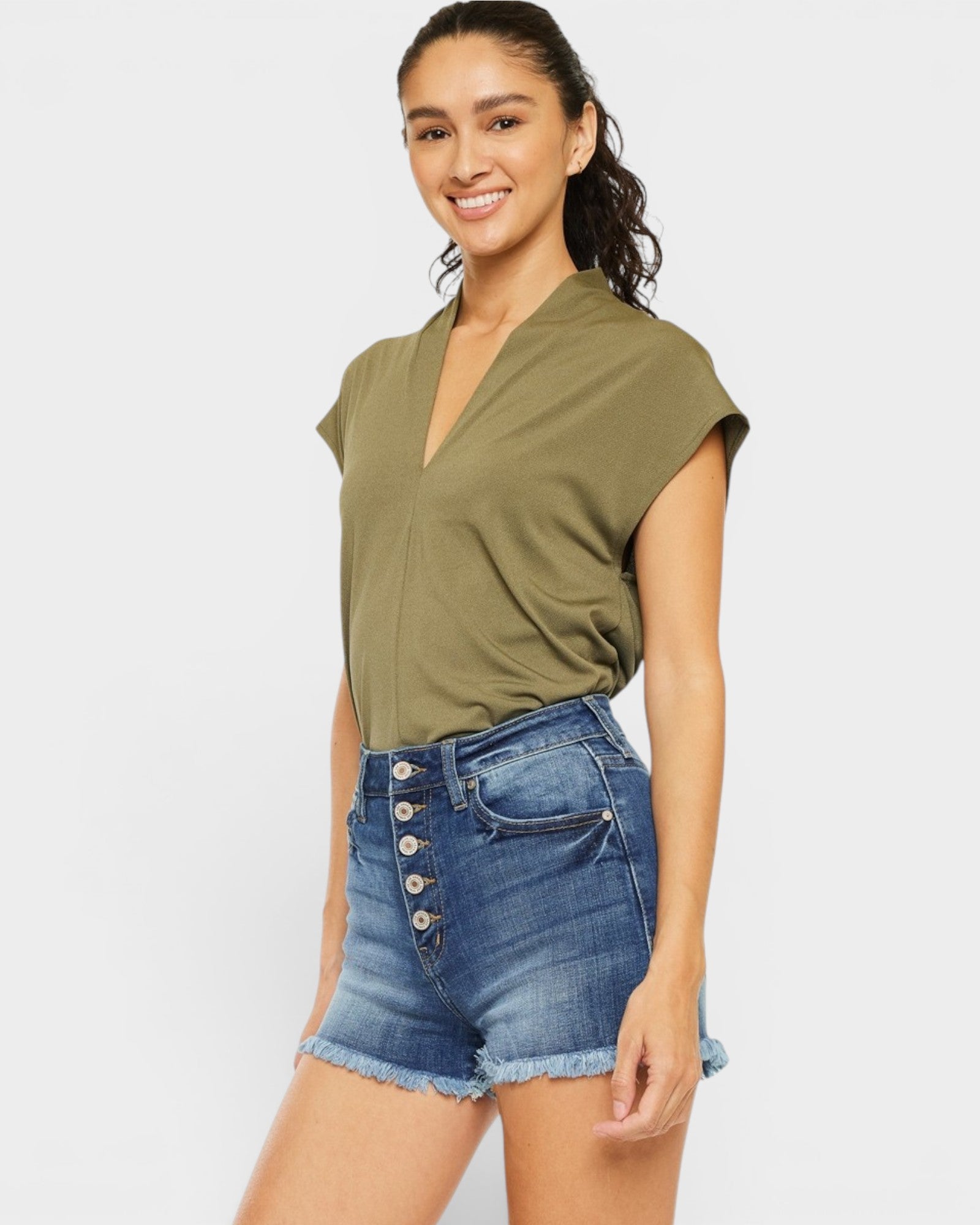 Woman wearing an olive green top and denim shorts on a white background