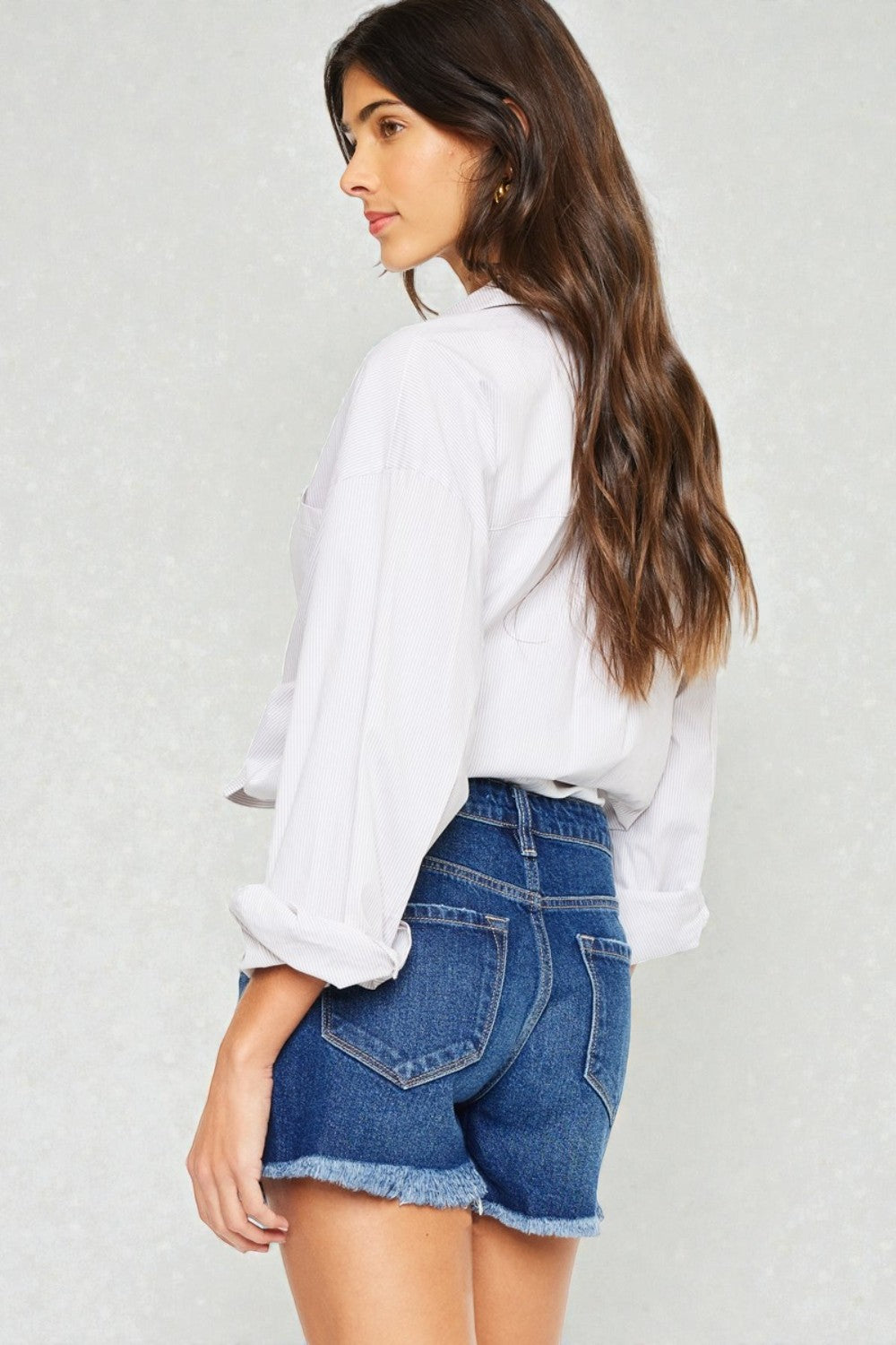 Woman wearing a white blouse and blue denim shorts on a plain background