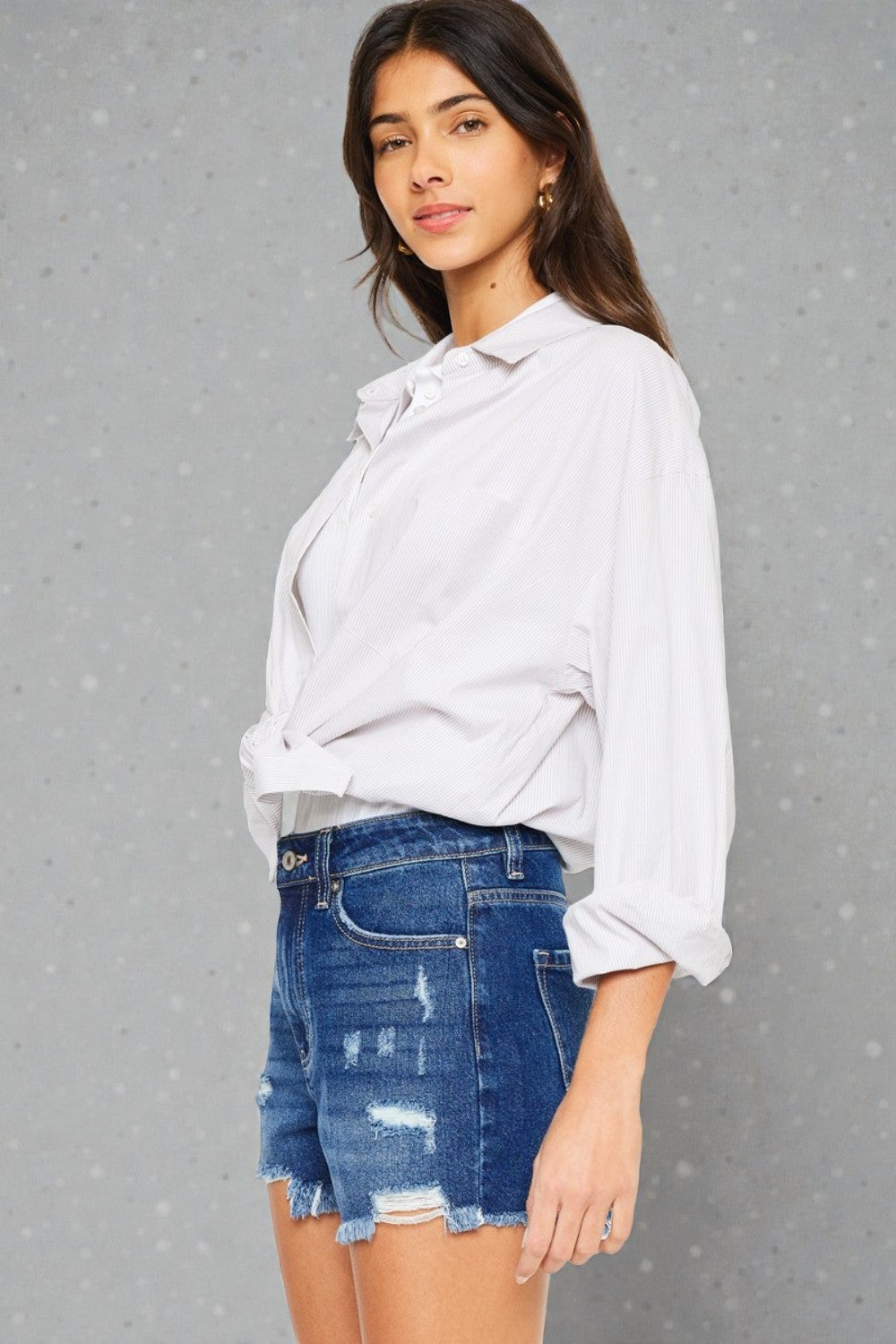 Woman wearing a white blouse and blue denim shorts against a gray background
