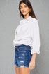 Woman wearing a white blouse and blue denim shorts against a gray background