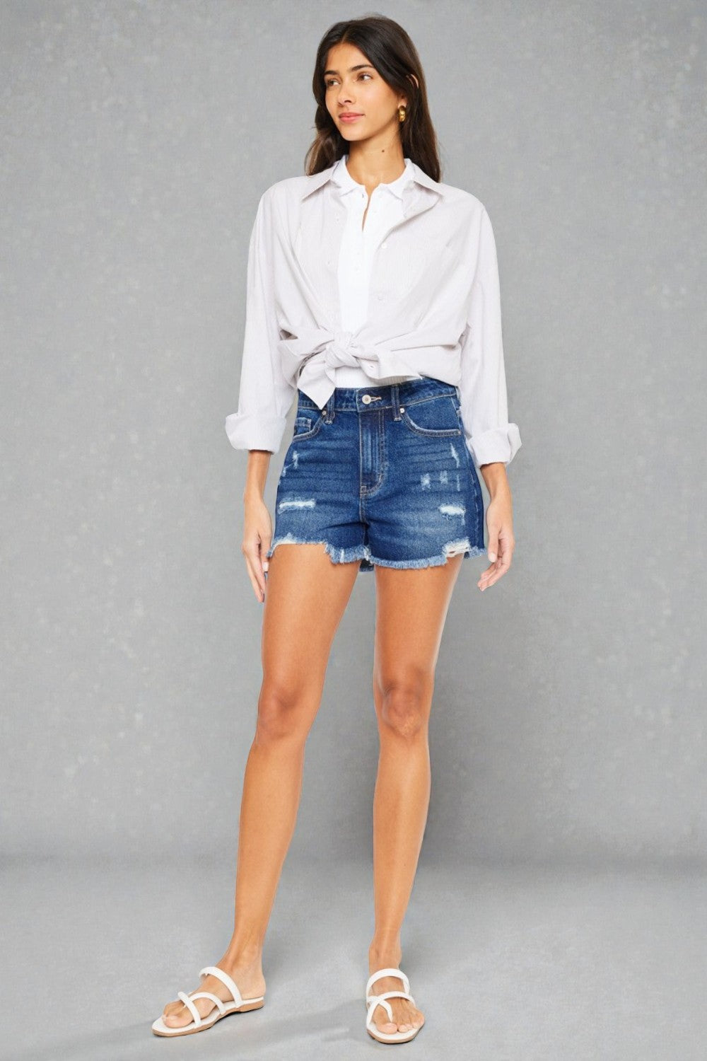 Woman wearing a white shirt and blue denim shorts on a gray background