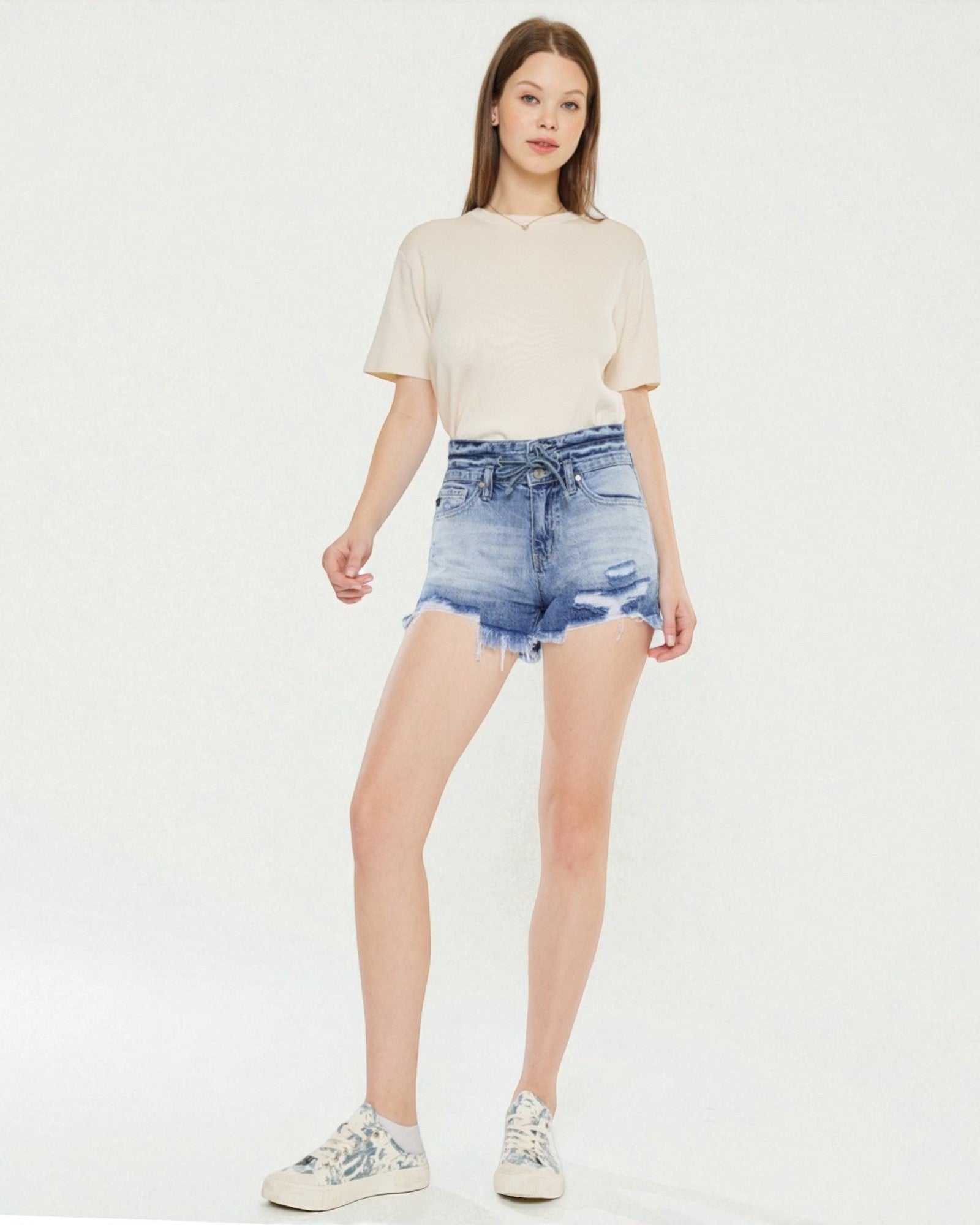 Woman wearing a beige top and denim shorts on a white background