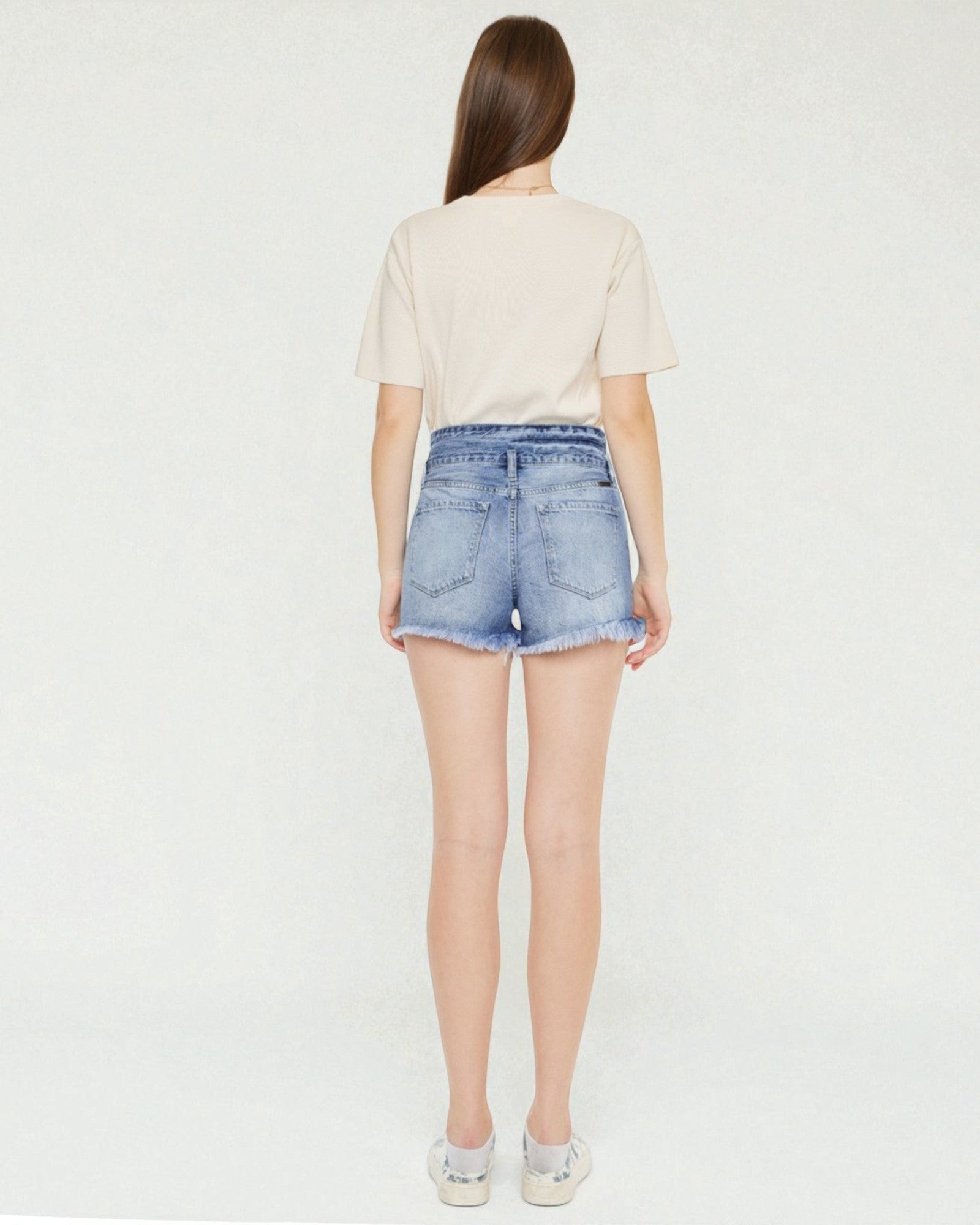 Person wearing a beige top and denim shorts on a white background